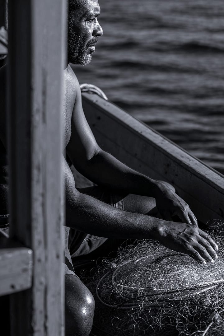 Black and white portrait of a Brazilian fisherman in a boat looking out at the sea titled Quando o Mar Fala, a Alma se Cala, from the Cotidiano series in the Brasil Profundo collection, by artist YSA.